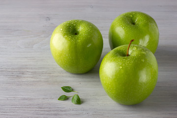 Green fresh apples and some basil leaves on wooden table close up