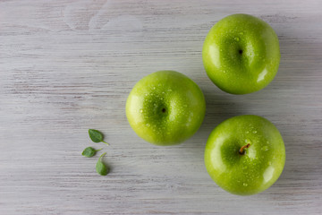 Green fresh apples and some basil leaves on wooden table close up, top view