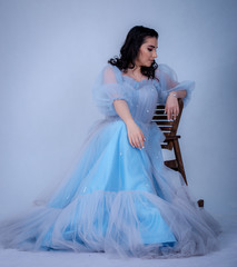 young beautiful model in the image of princesse ,cinderella dressed in a blue dress,sitting on a chair