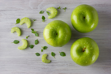 Green fresh apples, celery slices and some basil leaves on wooden table close up, top view
