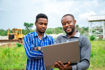 african agricultural businessmen, discussing using a laptop on a piece of land
