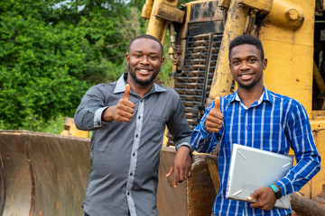 african business men giving thumbs up gesture, standing next to tractor