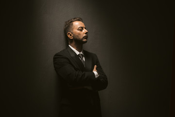 Fototapeta premium Lonely businessman feels depression. Sad man in black suit stands closed eyes with arms crossed in dark room. Stress concept. Business concept. Copy space for text at right side