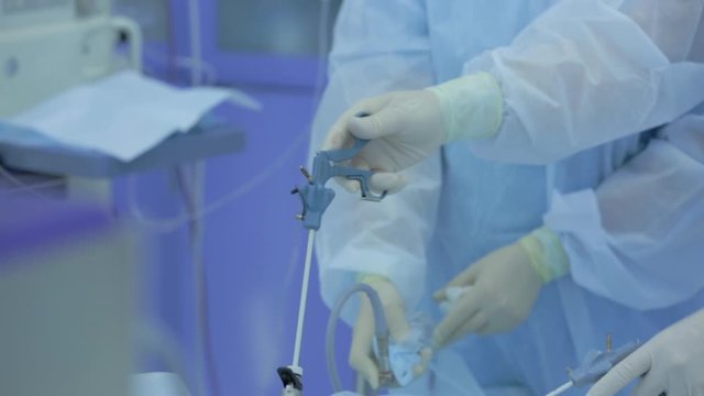 Close-up of surgeon's hands in operating room, real laparoscopic operation is performed, removal of tumor from abdominal cavity, punctures on abdomen, technologies, life saving, work with assistant