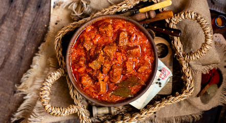 overhead shot of homemade tasty stewed meat in tomato sauce with vegetables. goulash in wooden bowl on rustic table  - obrazy, fototapety, plakaty