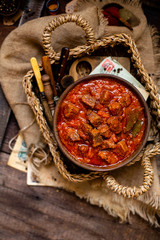 overhead shot of homemade tasty stewed meat in tomato sauce with vegetables. goulash in wooden bowl on rustic table 