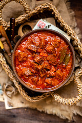 overhead shot of homemade tasty stewed meat in tomato sauce with vegetables. goulash in wooden bowl on rustic table 