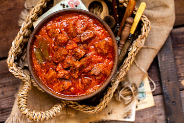 overhead shot of homemade tasty stewed meat in tomato sauce with vegetables. goulash in wooden bowl on rustic table 