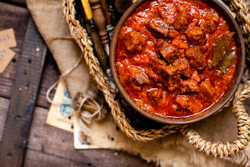 overhead shot of homemade tasty stewed meat in tomato sauce with vegetables. goulash in wooden bowl on rustic table 