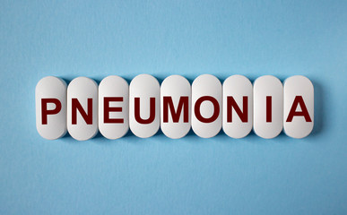 The word Pneumonia is written on white tablets on a blue background. Medical concept.