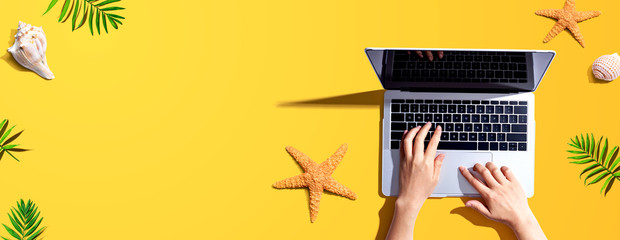 Person using a laptop computer with summer theme objects - flat lay