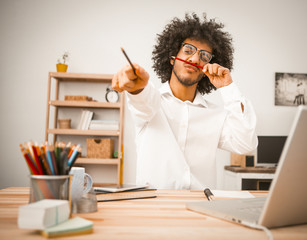 Creative man takes a break from work. Millennial guy having fun making a mustache by applying a...