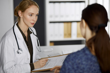 Friendly smiling female doctor and patient woman discussing current health examination while...
