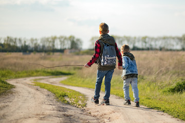 two brothers are walking along a dirt road and holding hands. Little travelers and explorers.