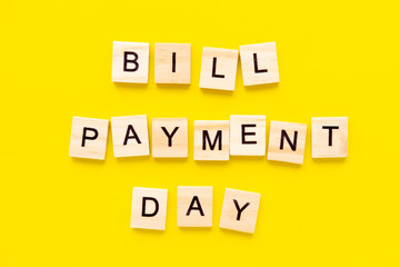 words Bill payment day. Wooden blocks with lettering on top of yellow background. finance concept.