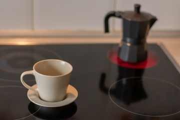 Cup of coffee on a ceramic hob and a coffee pot on an unfocused fire