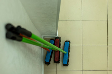 mops of different colors stand near the wall in a clean room. brushes for sweeping the floor stand near the wall. three brushes for the floor. clean indoors. There is no dirt in the building. 