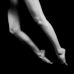 Fototapeta premium black and white photo of female legs standing on bent fingertips isolated on black background