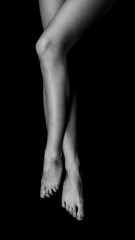 black and white photo of female legs crossed lying on a black void and pulling toes, top view isolated on black background
