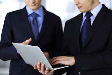 Fototapeta premium Business people discussing a presentation at meeting, standing in a modern office. Unknown businessman with a colleague search for some information at the laptop, lawyers at negotiation. Teamwork and