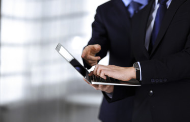 Business people discussing a presentation at meeting, standing in a modern office. Unknown businessman with a colleague search for some information at the laptop, lawyers at negotiation. Teamwork and
