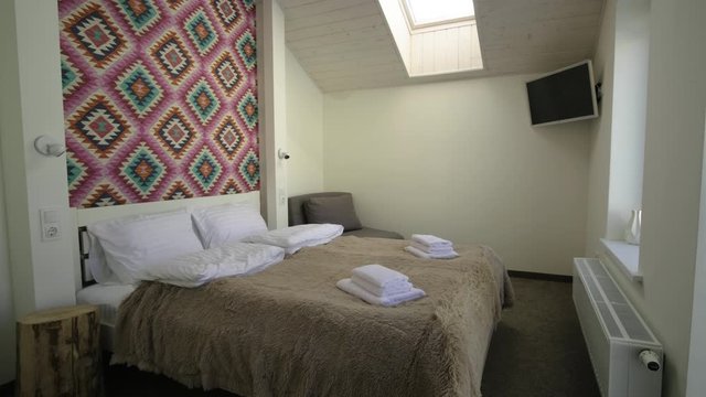 Interior of a spacious hotel bedroom on attic floor with fresh linen on a big double bed. Cozy contemporary mansard room in a modern house.