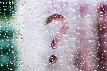 Drops of morning summer rain on a fogged window with a question mark drawn on a blurred background of nature in the daytime. Summer vacation and travel concept