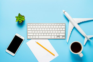 Keyboard, flower, airplane, cup with tea or coffee, a blank sheet and a pencil on a blue background. Concept of travel planning, buying airline tickets online, selling air tickets. 