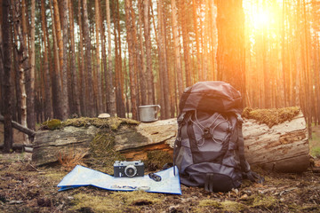 Tourist backpack, metal mug, camera and map in the forest. Concept of a hiking trip to the forest or mountains