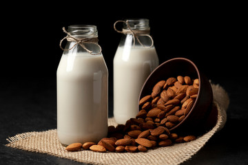almond milk in glass bottles on a dark background with nuts, vegetarian milk without sugar and lactose