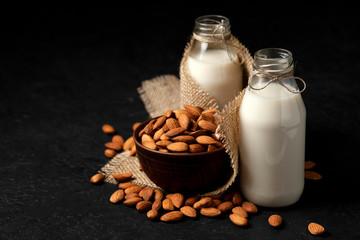 almond milk without sugar and lactose in bottles with sprinkled nuts, vegetarian milk drink on a black table