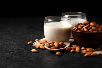 two glasses of almond milk with nuts on a dark black table, vegetarian milk drink, dairy product with almonds