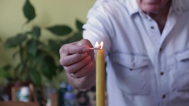 Old Man Lighting A Candle. Senior man in blue jeans shirt holding matches in his hands and lighting a candle.