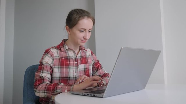 Slow motion: woman in red plaid shirt using laptop, having video chat with friends in grey room. Communication, conference, self isolation, quarantine, conference, safety, online technology concept