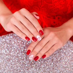 Obraz na płótnie Canvas Female hands with fashion glamour manicure in red colours with heart design on nails on sparkling background