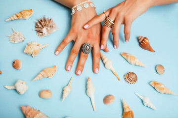 beautiful woman hands with pink manicure holding sea shells, lot of rings on fingers on blue...
