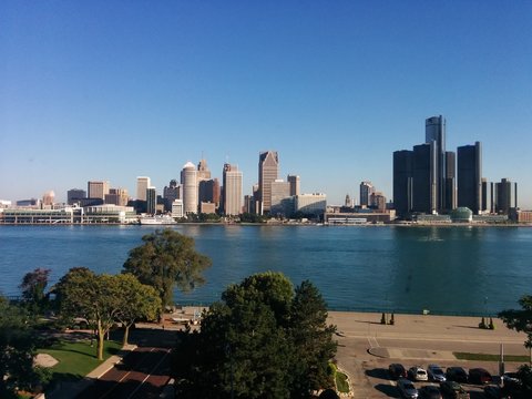 Downtown Detroit, Michigan, USA - City skyline with a mixture of modern and historic skyscrapers beneath a blue sky with the Detroit River and a park in the background. This was taken in Windsor, CA.