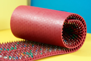 Massager in the form of a red carpet with spikes, metal needles, lie on a yellow-blue background....