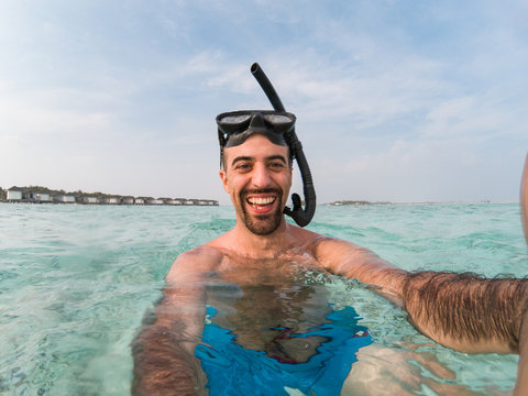 Happy man with snorkeling equipment taking a selfie at Maldives resort - Water level view of a smiling young man at summer destination - Tropical beach vacation at ocean paradise - Action camera photo