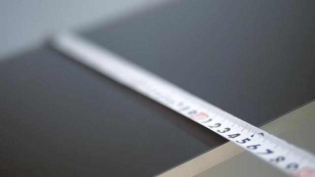 A man measures the size of a black glossy tile with a tape measure. Macro. Closeup. Shallow depth of field. Focus pull
