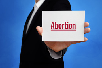 Abortion. Lawyer holding a card in his hand. Text on the board presents term. Blue background. Law, justice, judgement