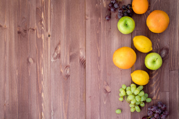fruits on the right edge of a mocha color wooden background.  lemon, orange, grapefruit, red grapes, green grapes