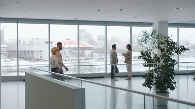 Zoom-in of man and woman business people talking in lobby discussing work while colleagues are walking around. Cooperation and workplace concept.