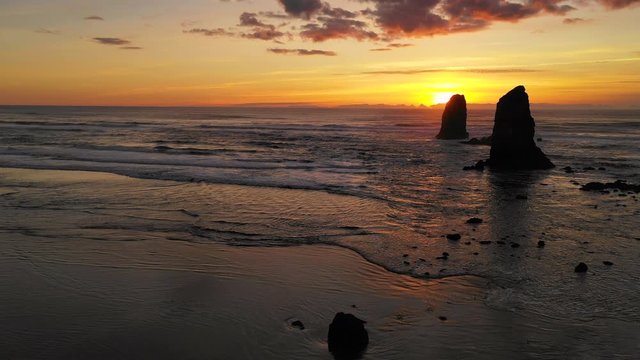People Walk Cannon Beach as Pacific Ocean Waves Reflect Sunset Glow