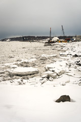 Big pieces of ice loosing and melting (floes) next to Port of Anchorage Small Boat Launch. Stevedore and cranes in the back. Winter in Knik Arm, Alaska.