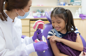 asian woman dentist with smiling face teaching young child how to brush teeth and take care of...
