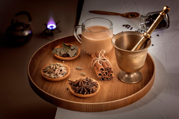 Obraz na płótnie Canvas Masala tea in a glass cup and a natural mixture for its preparation - star anise, cinnamon sticks, cardamom, bay leaf, pepper and pepper on a wooden dish. Low key