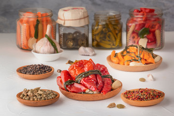 Fermented red hot peppers to enhance immunity with spices on a light wooden table against a background of glass jars with pickled products