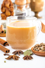 Masala tea in a glass cup and a natural mixture for its preparation - star anise, cinnamon sticks, cardamom, bay leaf, pepper and pepper on a white wooden table