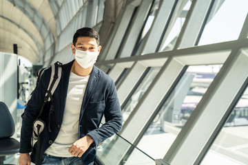 Asian traveler business man wearing face mask waiting to board into airplane, standing in departure terminal in airport. Male passenger traveling by plane transportation during covid19 virus pandemic.